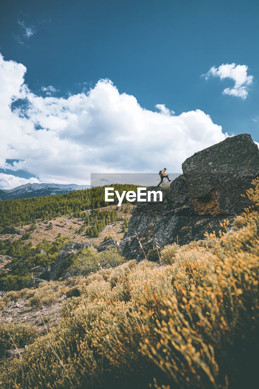 Man climbing rock on landscape against sky