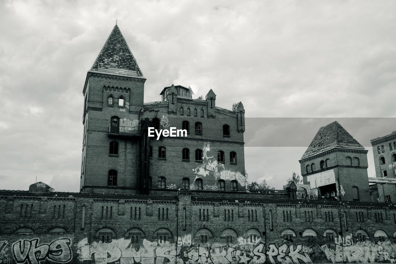 Low angle view of graffiti on old building against cloudy sky