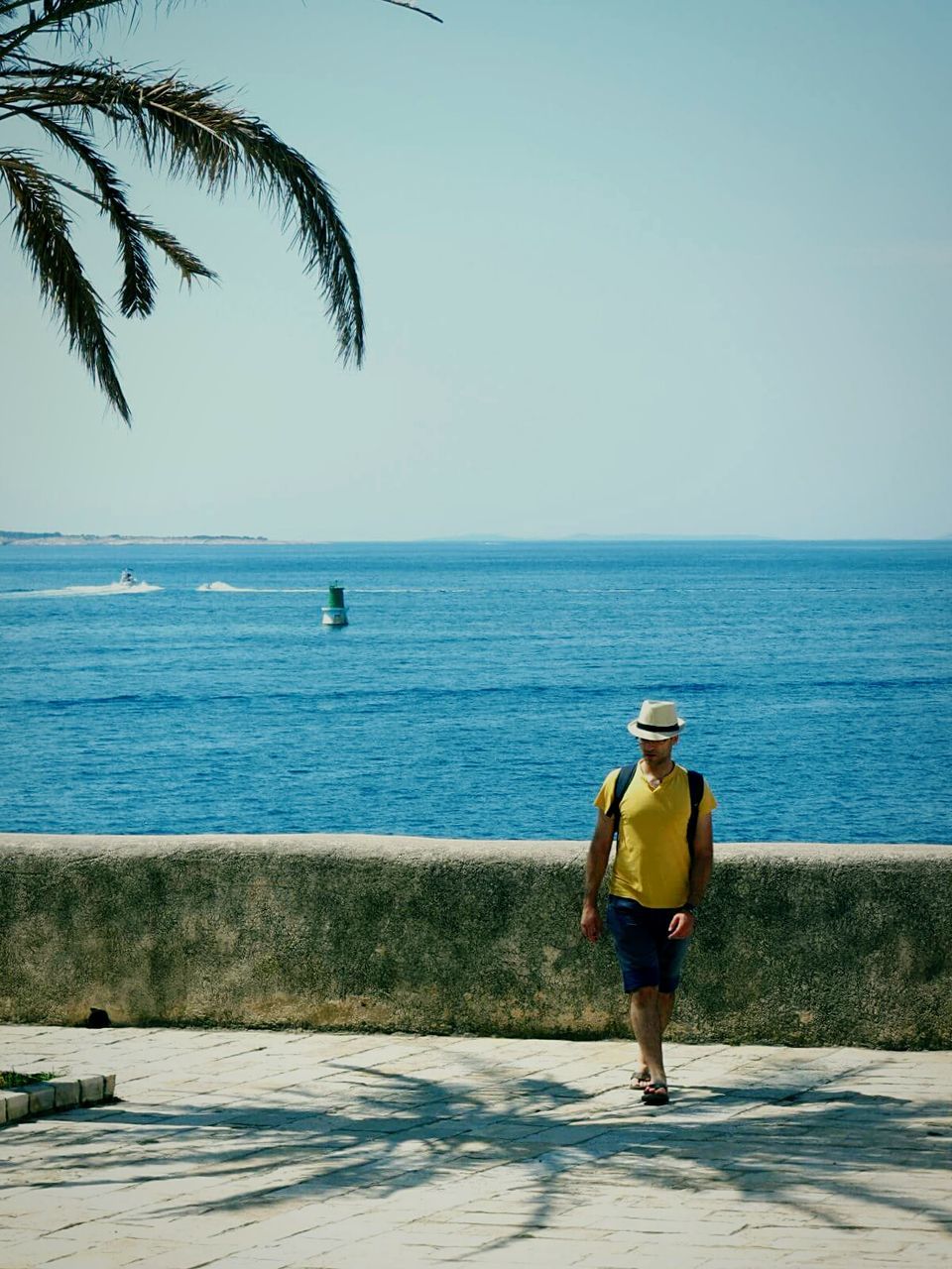 Full length of man walking on promenade by blue sea against clear sky