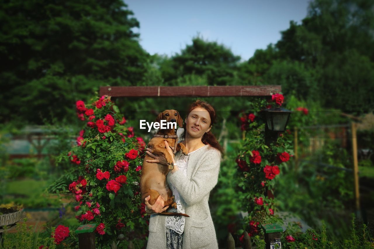 Portrait of smiling woman with dog standing against flowering plant