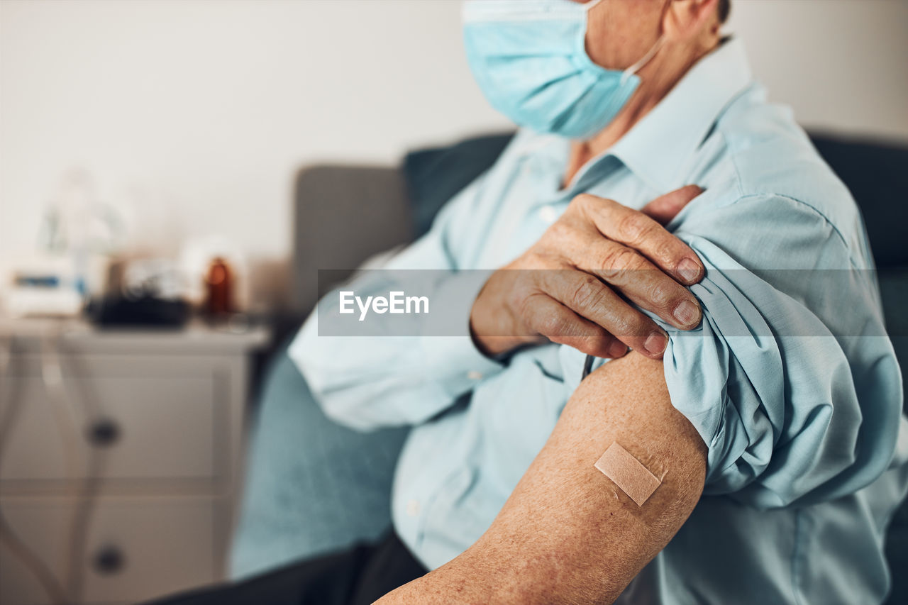 Senior man patient holding shirt sleeve up with a plaster in place of injection of vaccine. covid-19