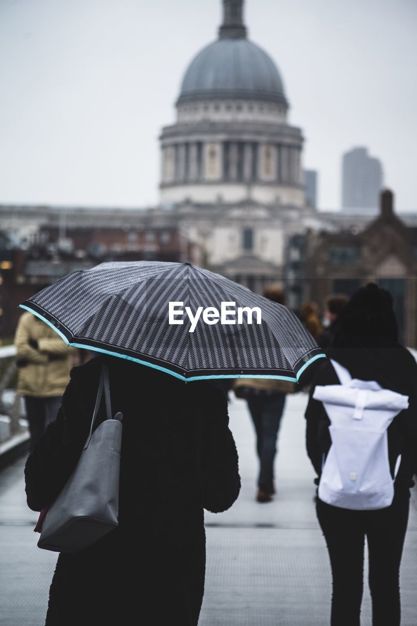 Rear view of woman walking with umbrella against historic building