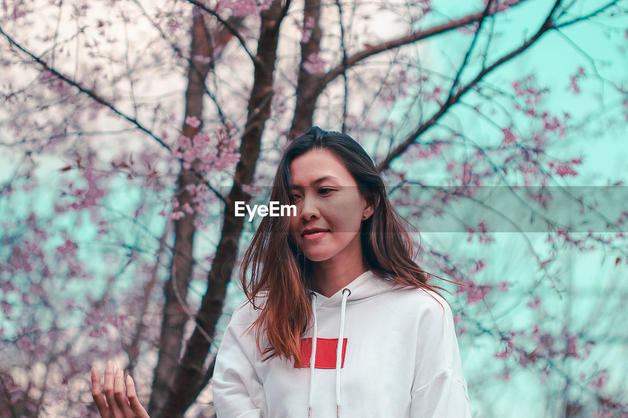 PORTRAIT OF BEAUTIFUL YOUNG WOMAN STANDING AGAINST PLANTS