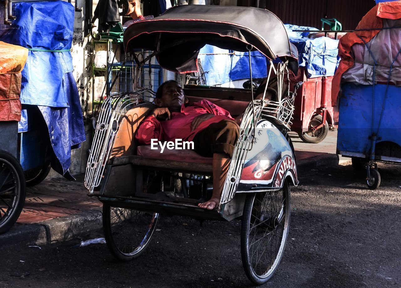 Man sleeping in pedicab on road