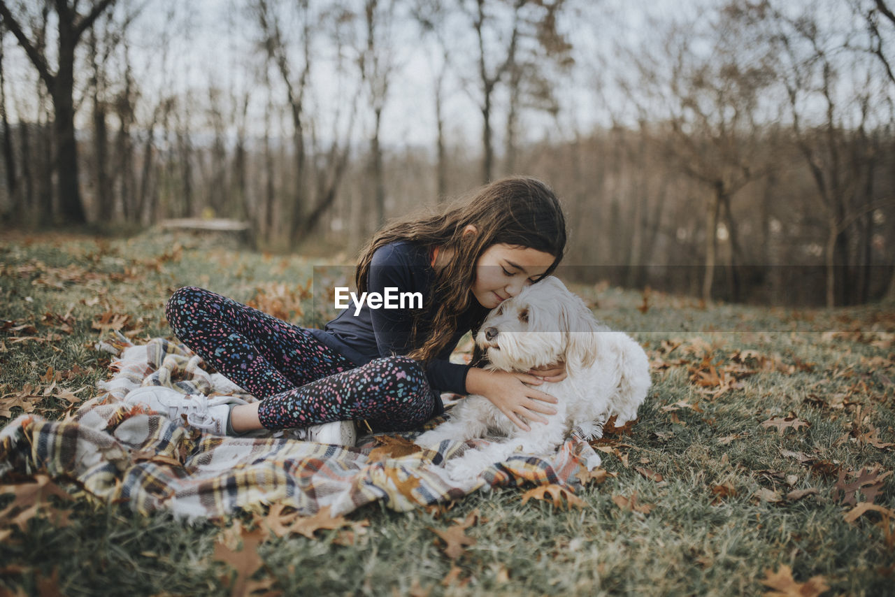 Girl embracing dog while sitting on land