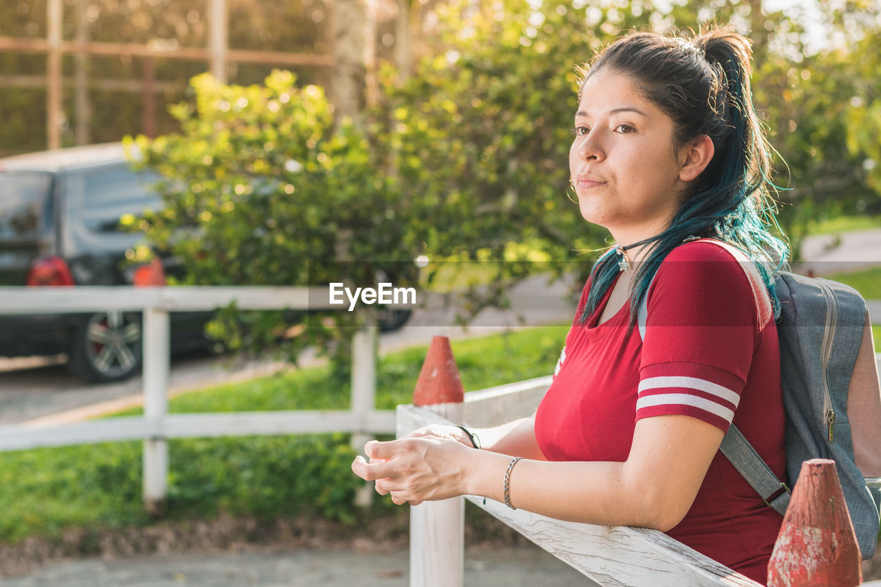 Beautiful young latina college girl, waiting for a person next to a wooden fence, dressed in red 