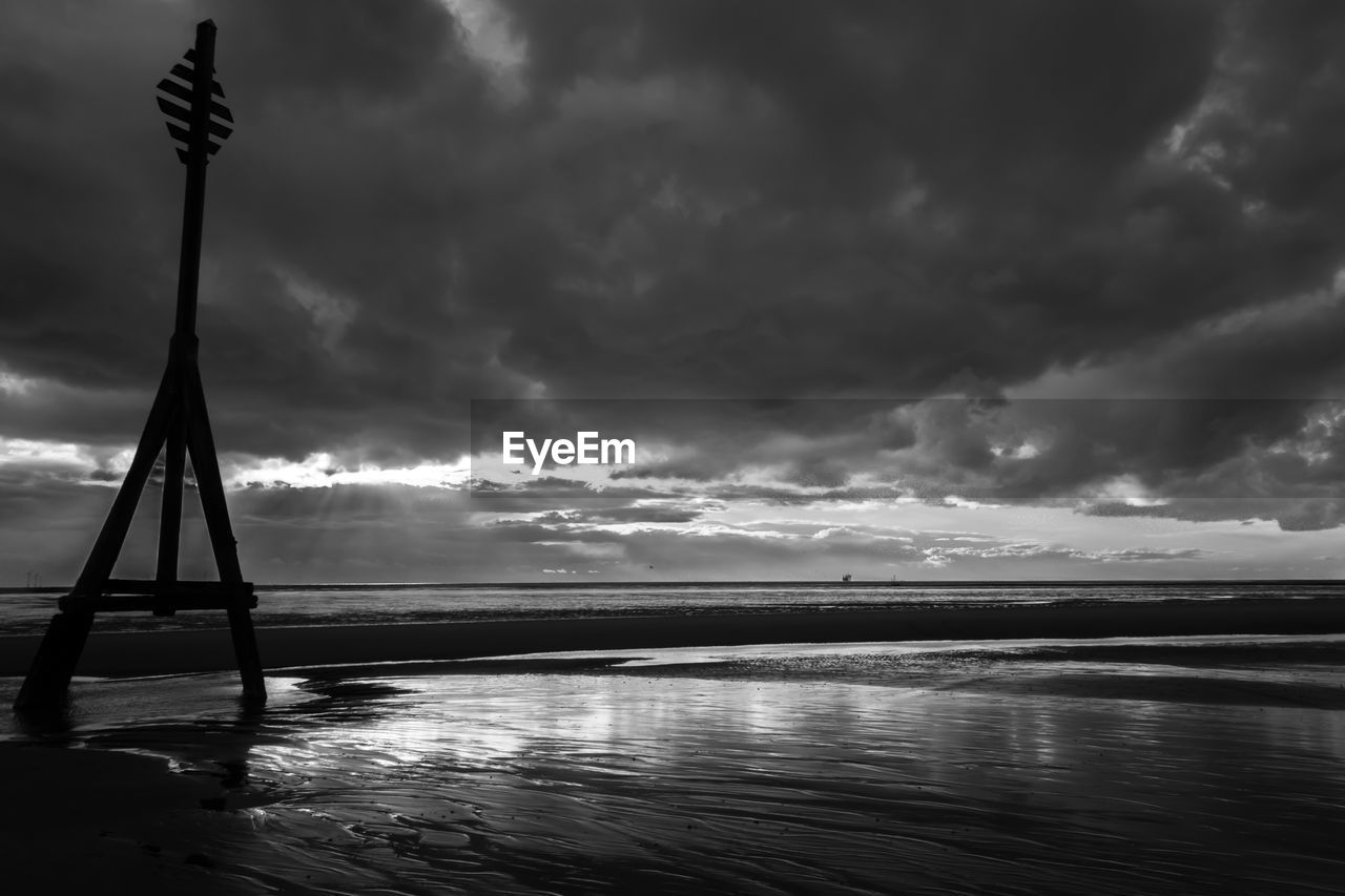 Silhouette pole at beach against cloudy sky