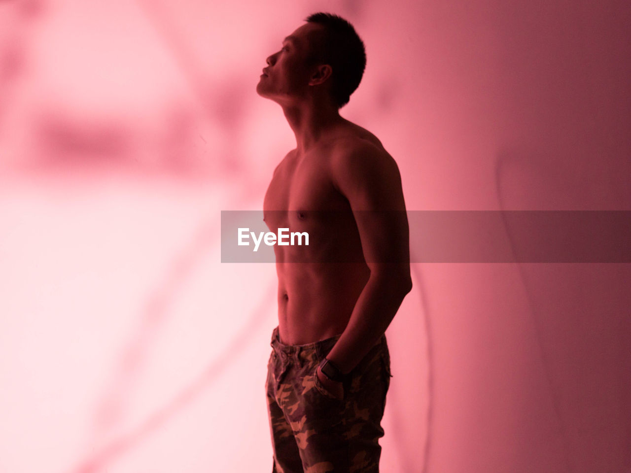 Side view of shirtless man standing against pink background