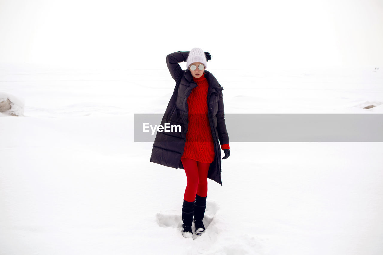 Woman stands in a snowy field in a jacket and sunglasses
