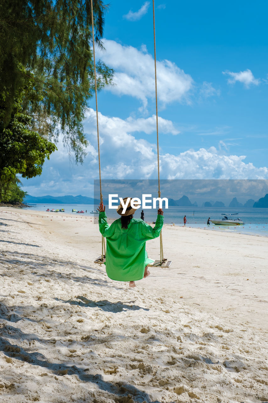 full length of boy swinging at beach against sky