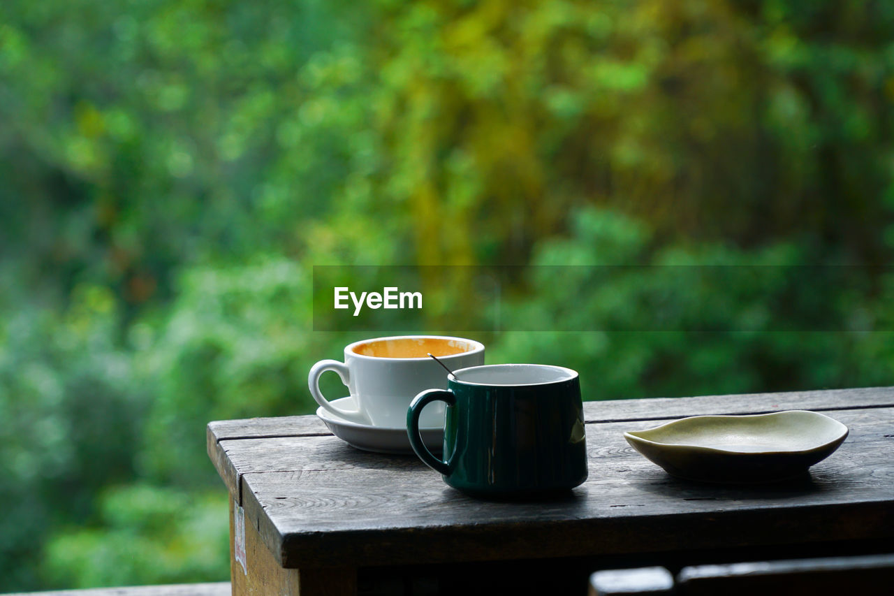 Close-up of coffee cups on wooden table against window