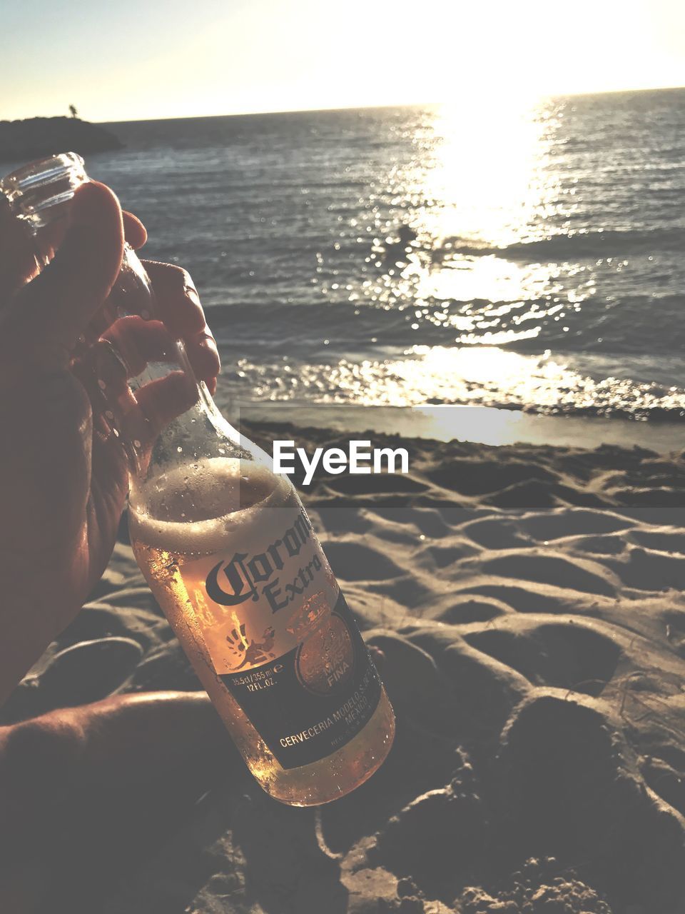 CLOSE-UP OF HAND HOLDING BOTTLE AT BEACH