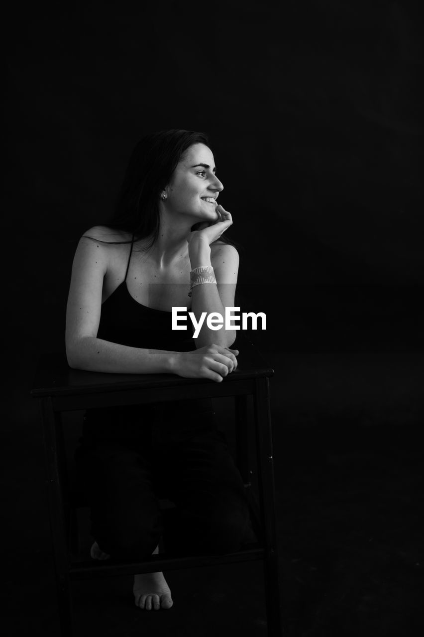 Portrait of young woman sitting against black background