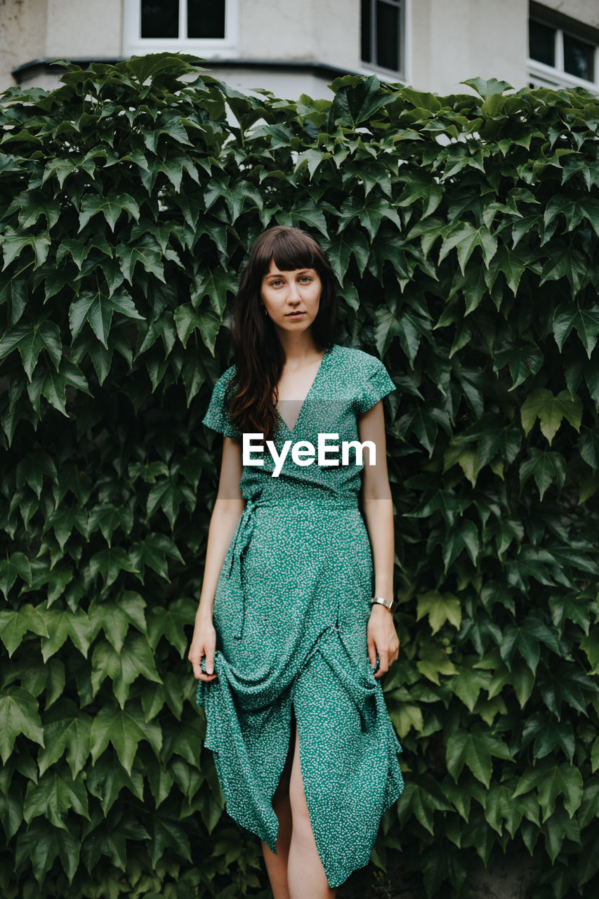 Portrait of beautiful woman standing against green leaves