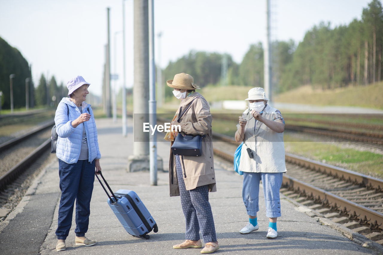 Three old senior women on  platform waiting for the train and wearing a face mask during a pandemic