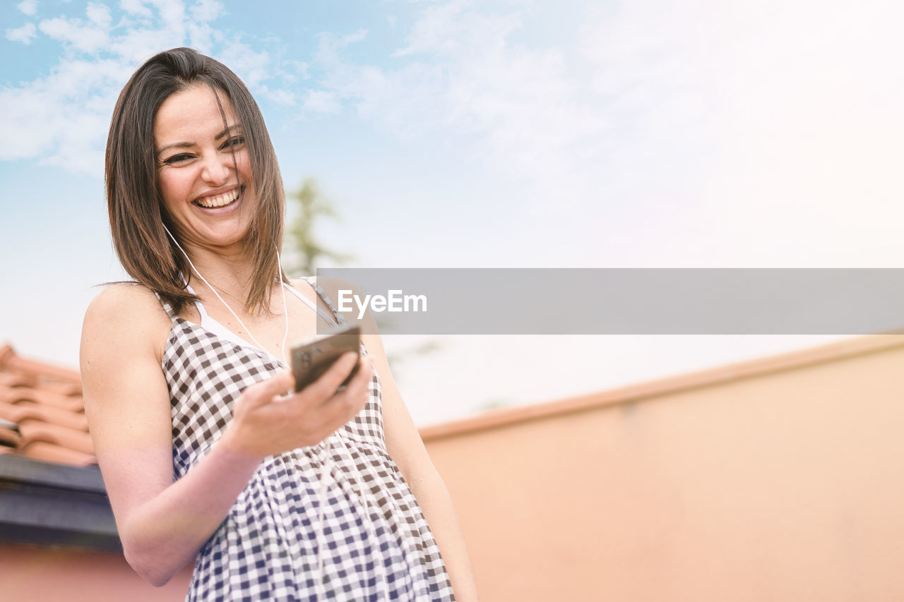 Portrait of smiling woman using mobile phone against sky