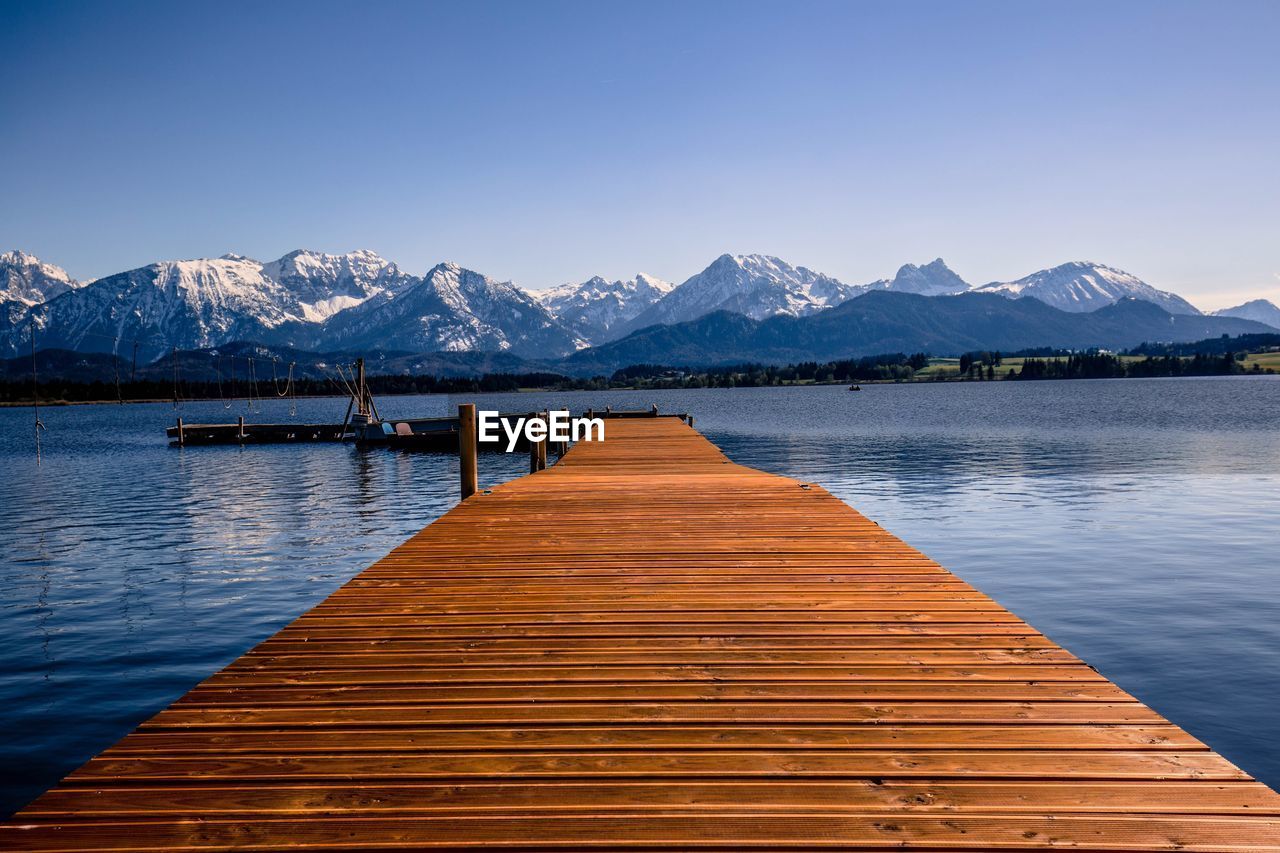 Wooden pier over lake against snowcapped mountains