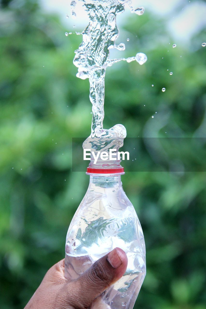 Close-up of hand holding bottle against water