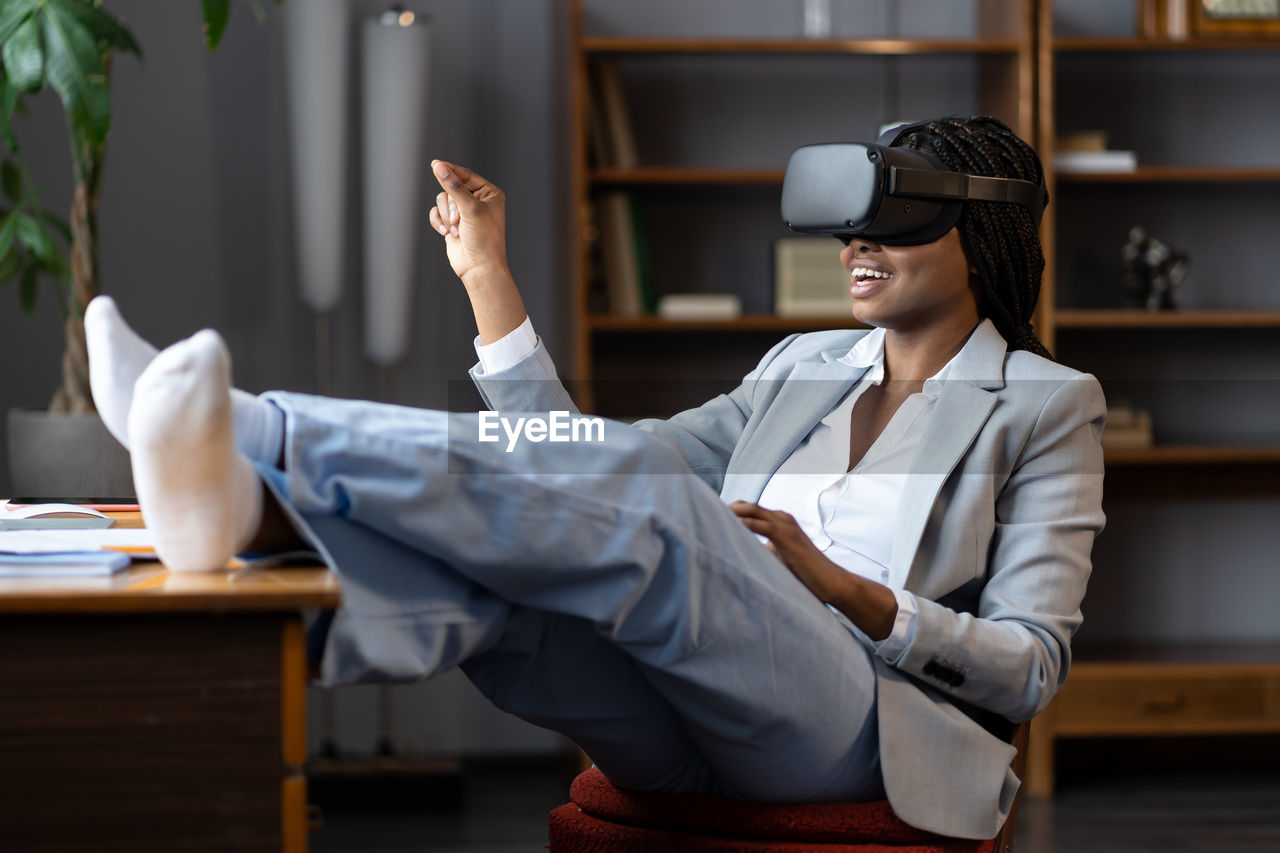 Curious afro businesswoman in vr goggles headset touching 3d virtual objects sit at office workplace