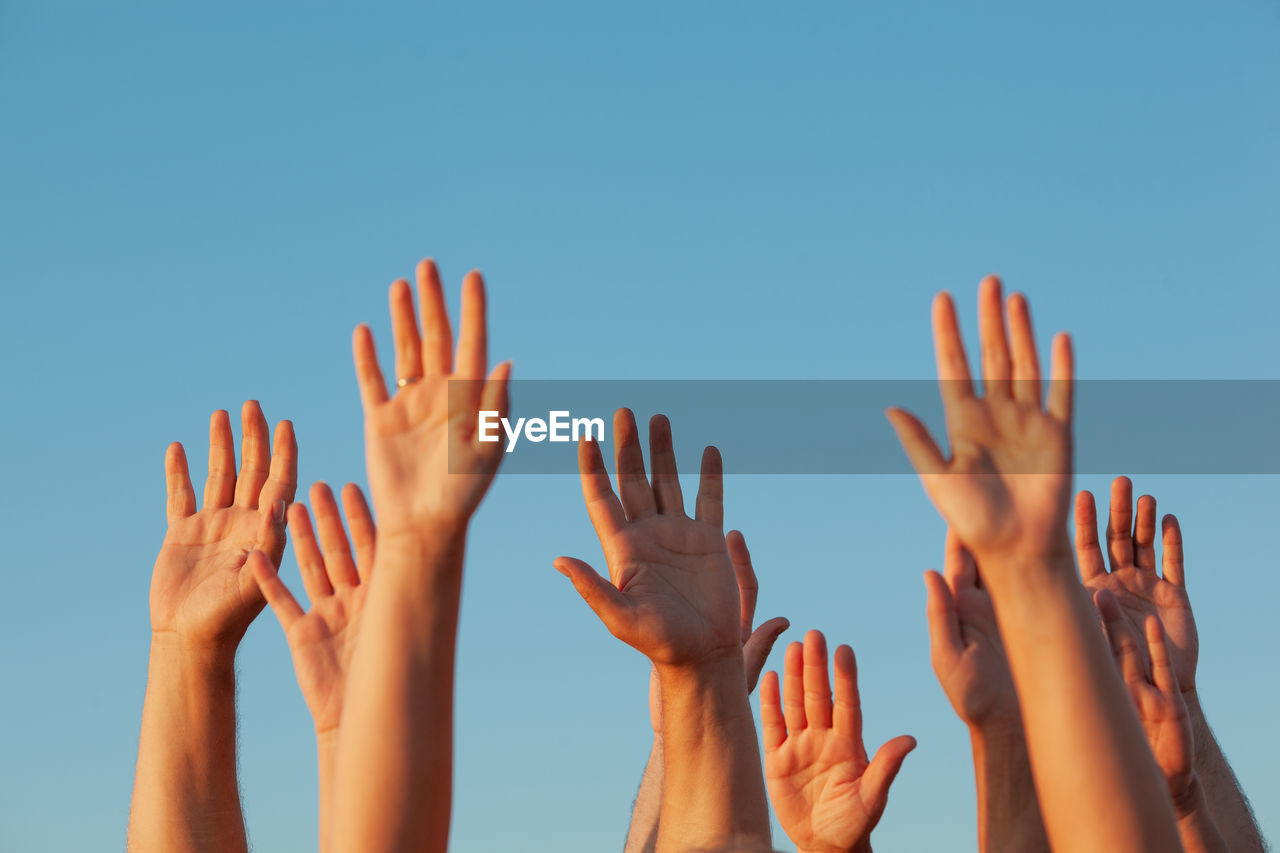 Cropped image of people with arms raised against clear sky