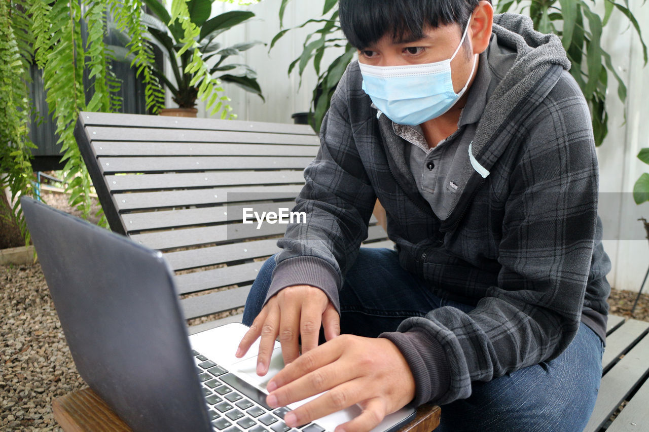 Masked asian man working online in shady shop off-site work concept