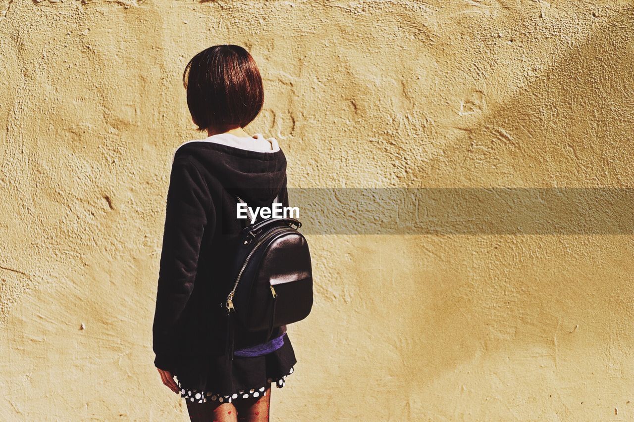 Rear view of woman with backpack standing against wall