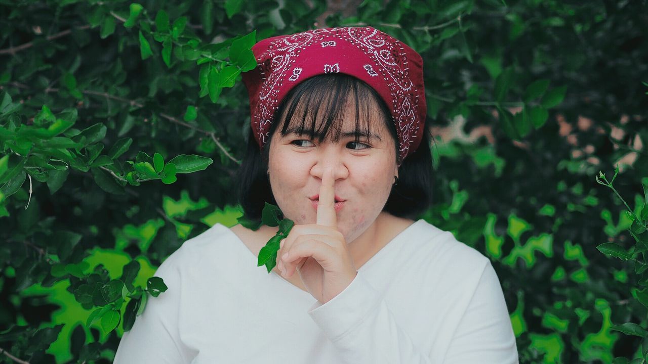 Close-up of young woman with finger on lips against plants