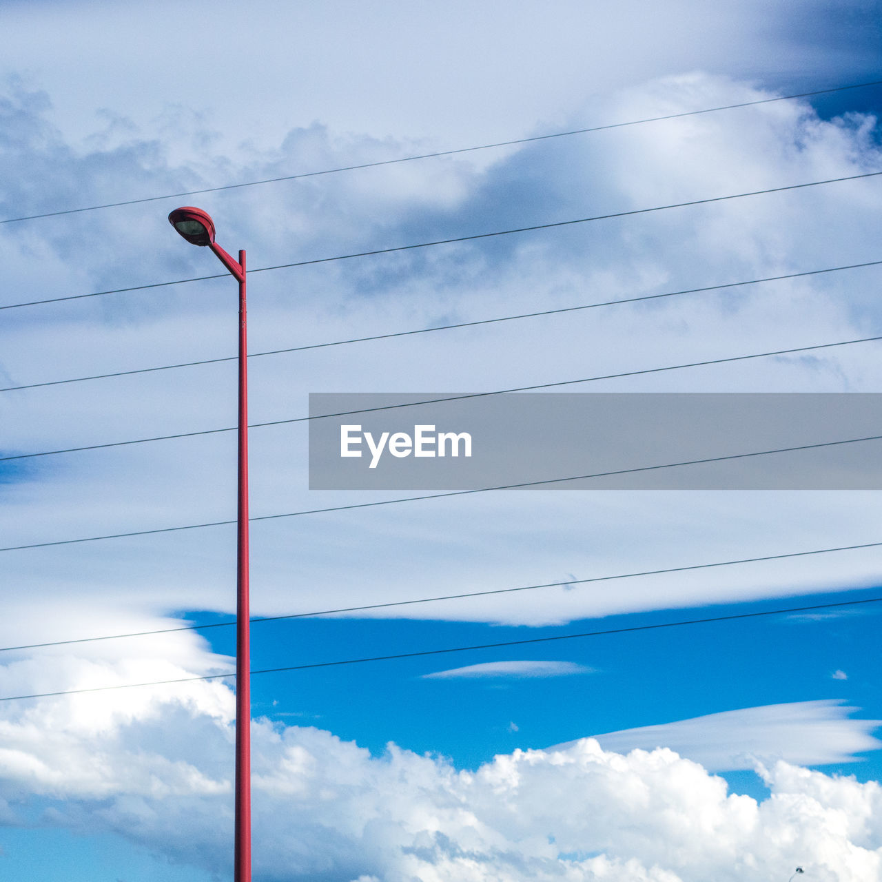 Low angle view of street light and power cables against cloudy sky