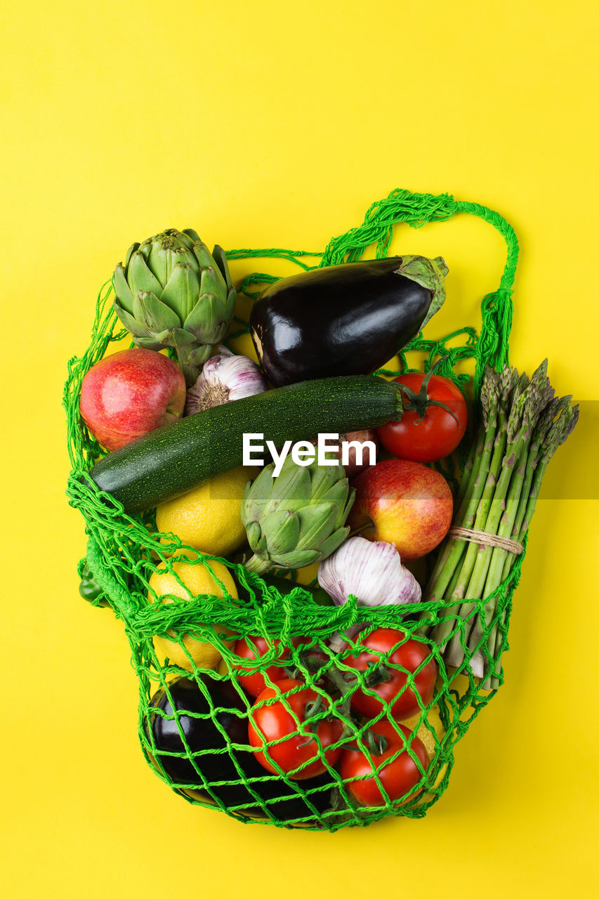 Textile mesh bag with produce, fruits and vegetables on yellow background. zero waste, eco-friendly