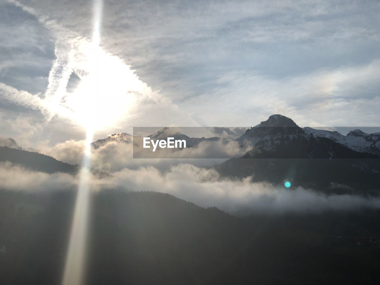 SUNLIGHT STREAMING THROUGH CLOUDS OVER MOUNTAIN