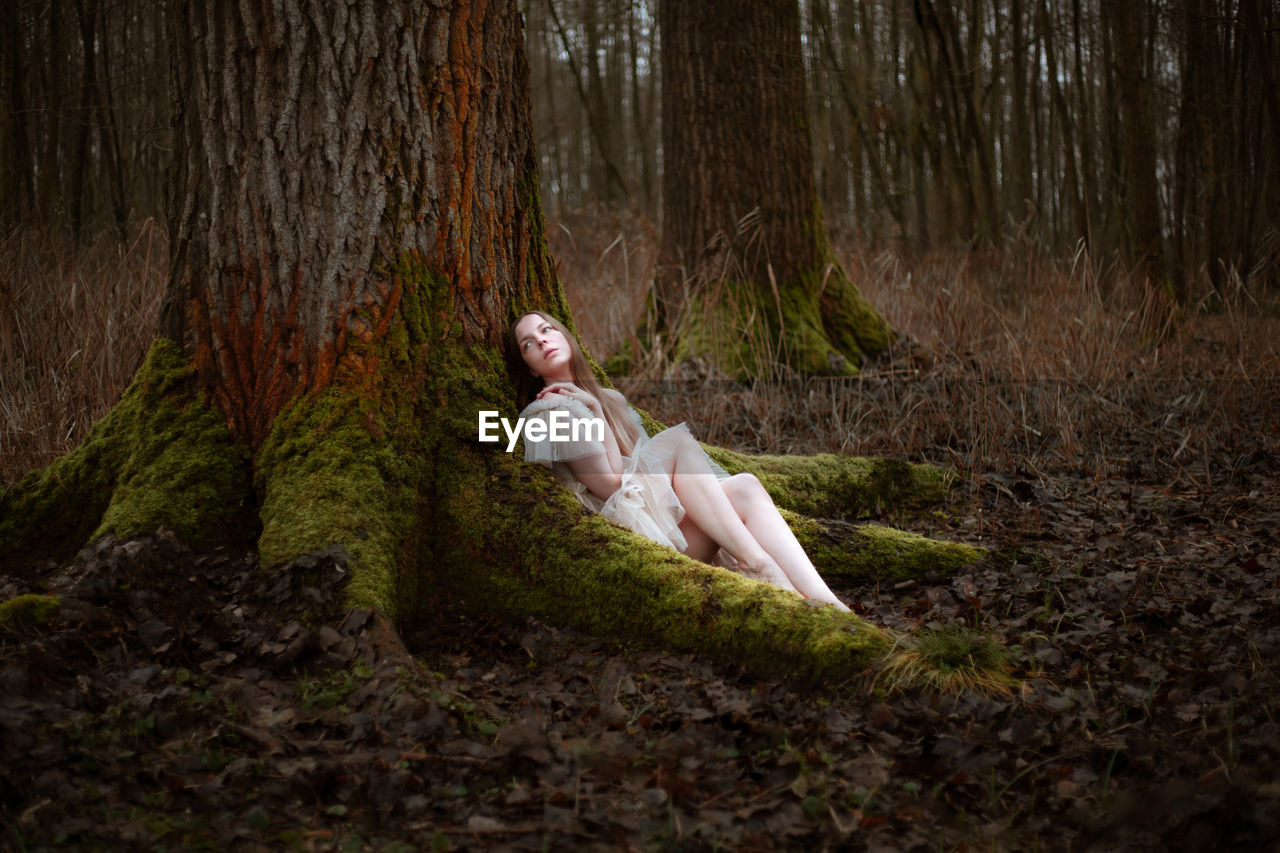 Side view of woman sitting in forest covered with moss