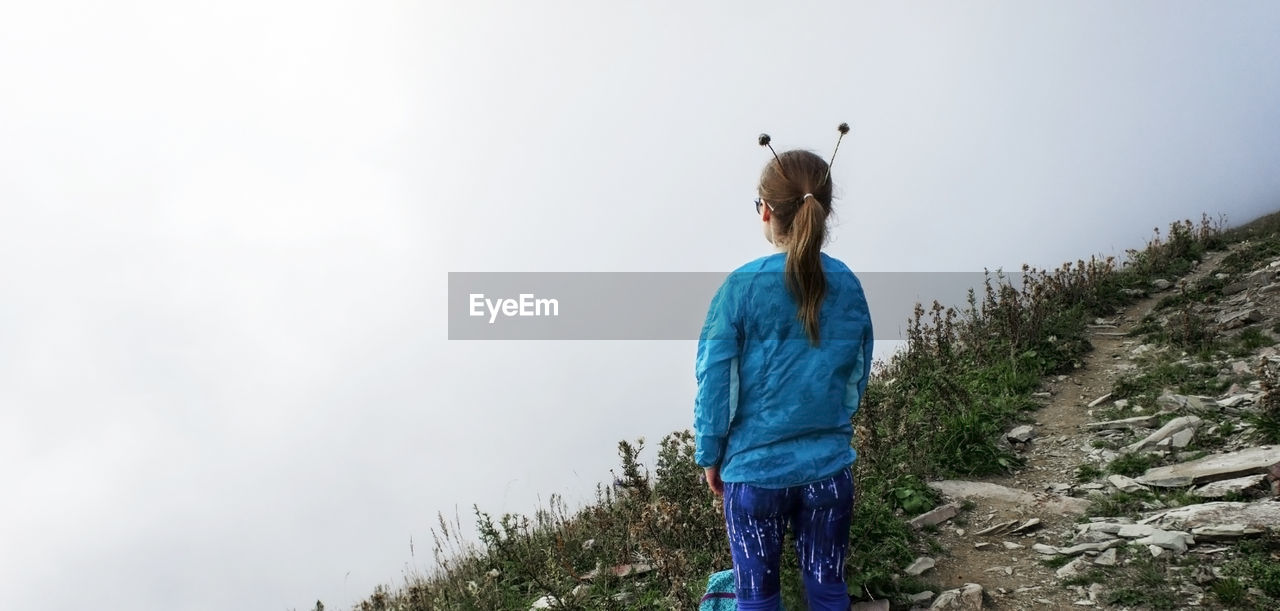 Girl from the back with plant horns on her head  in fog in mountains. fun concept, hiking, trekking