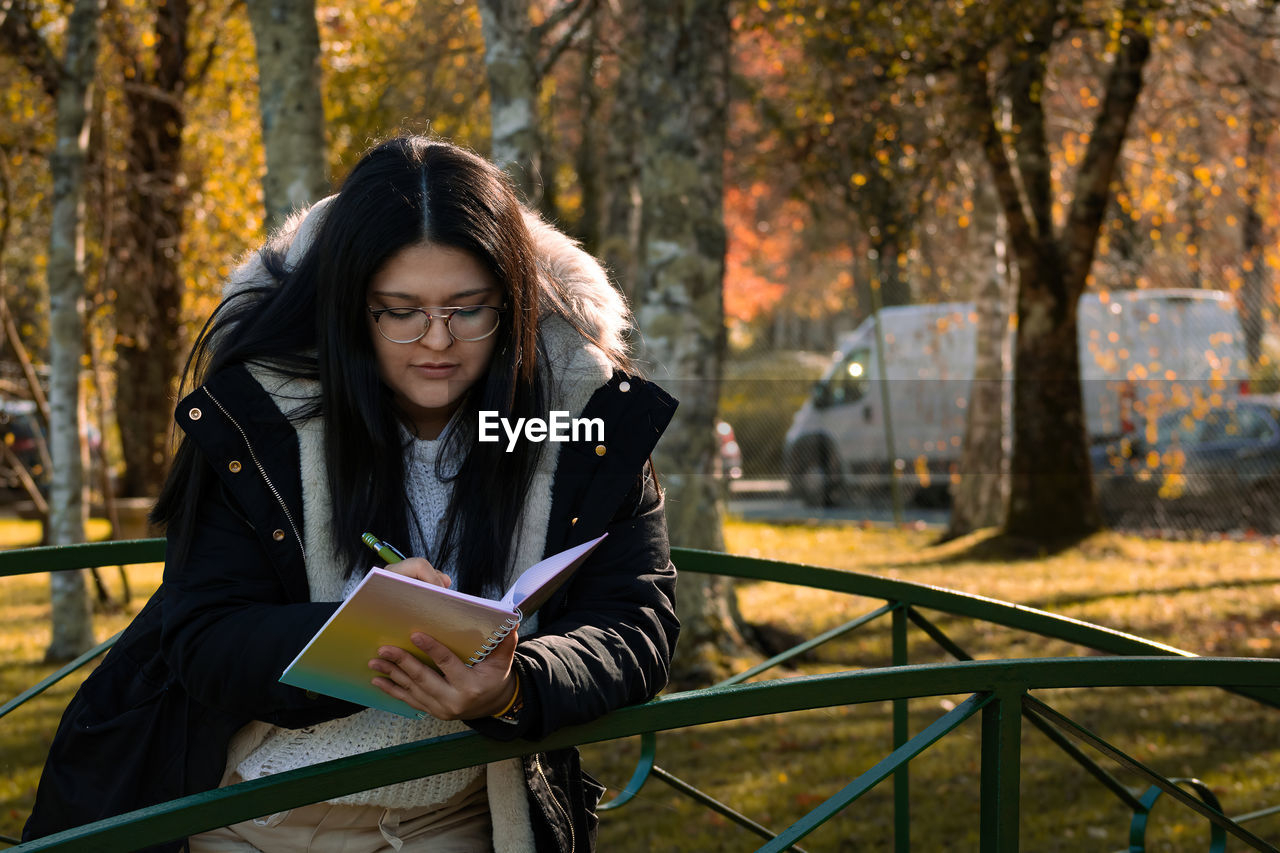 Woman studying in the park reading. woman taking notes in notebook.