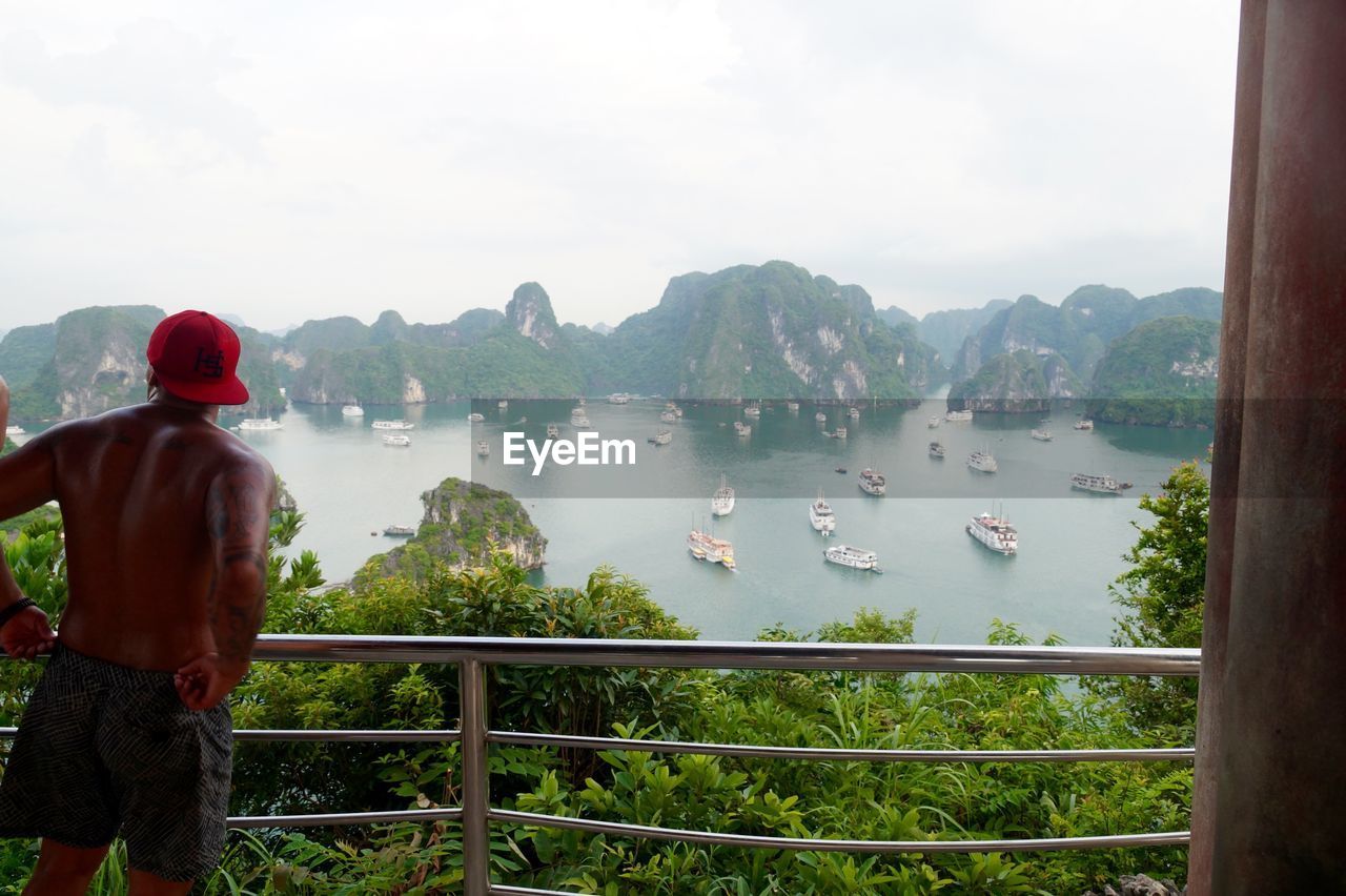 REAR VIEW OF MAN IN LAKE AGAINST MOUNTAINS