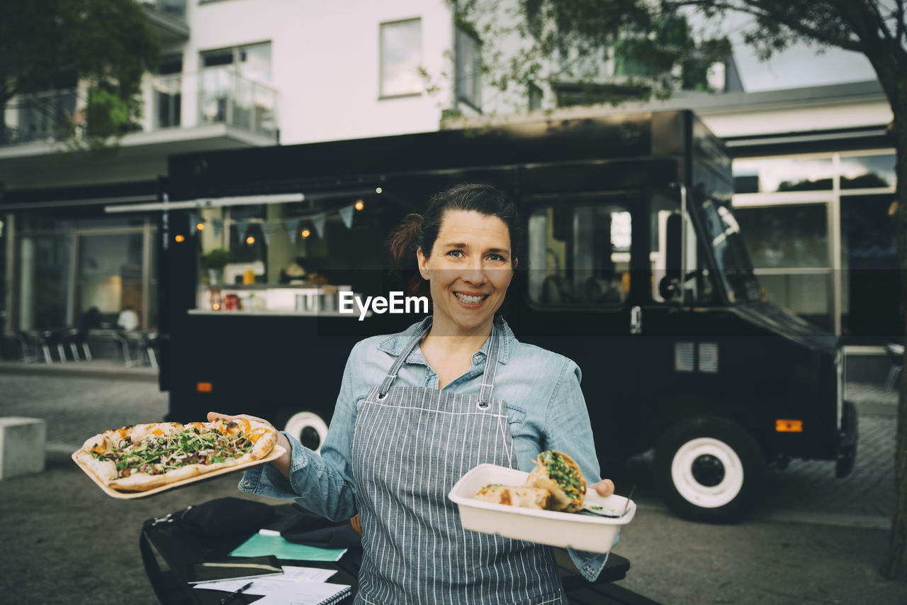 Portrait of smiling female owner with indian street food against commercial land vehicle