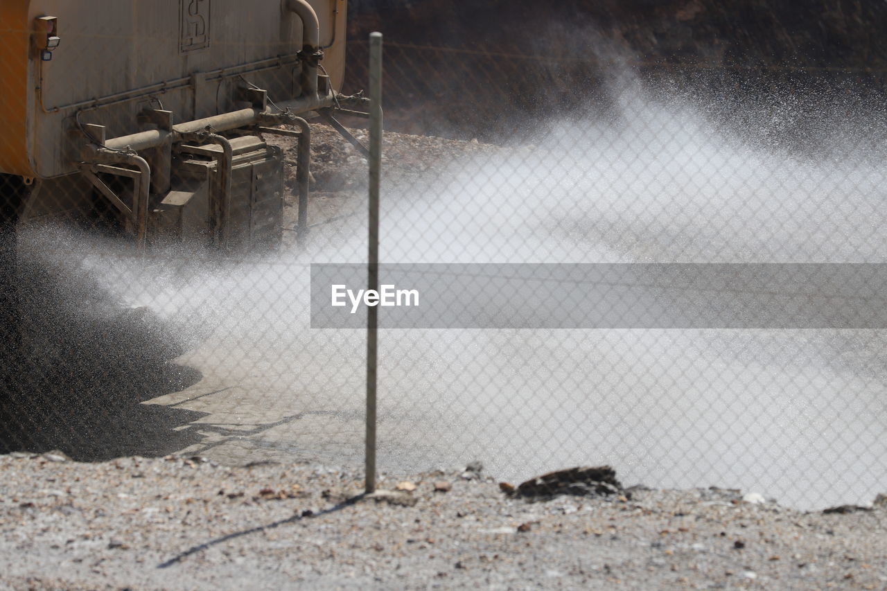 Full-frame view of spray from mining vehicle behind chain link fence