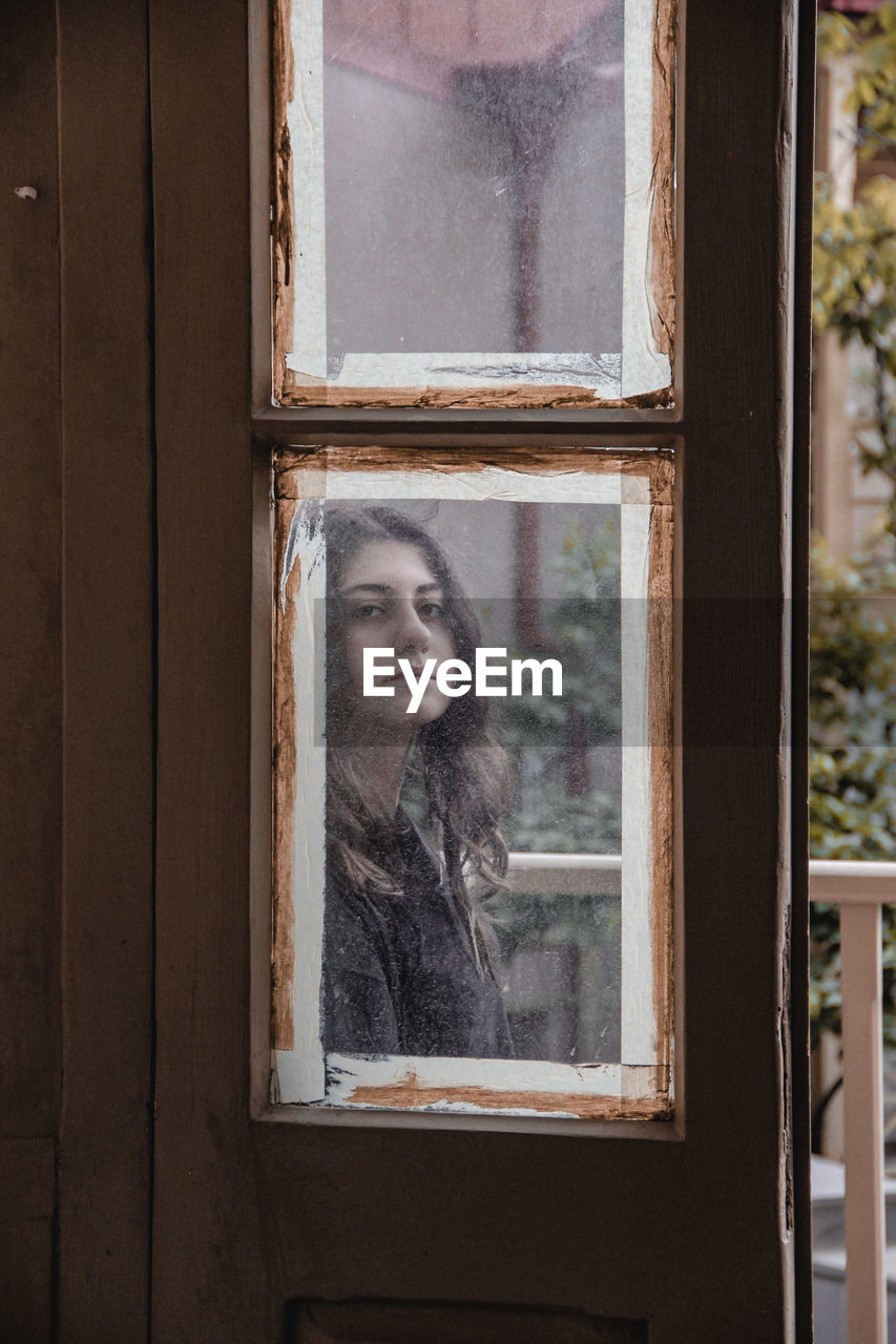 PORTRAIT OF YOUNG WOMAN IN WINDOW