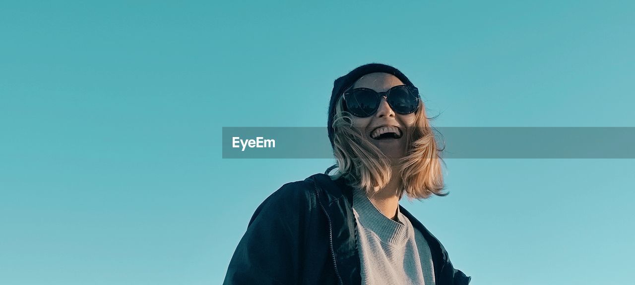 Portrait of young woman wearing sunglasses against clear blue sky