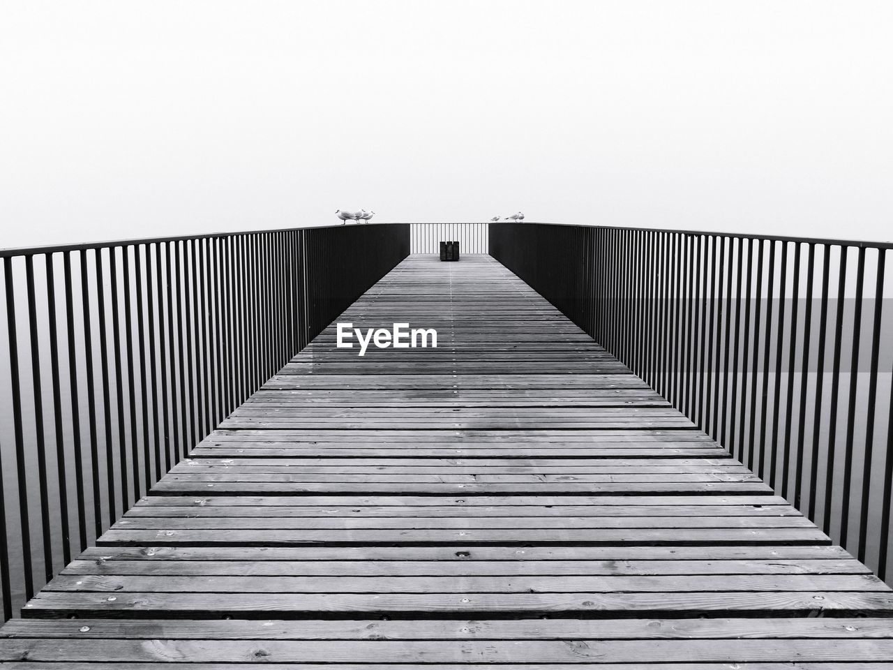 Wooden footbridge on pier against fogy sky