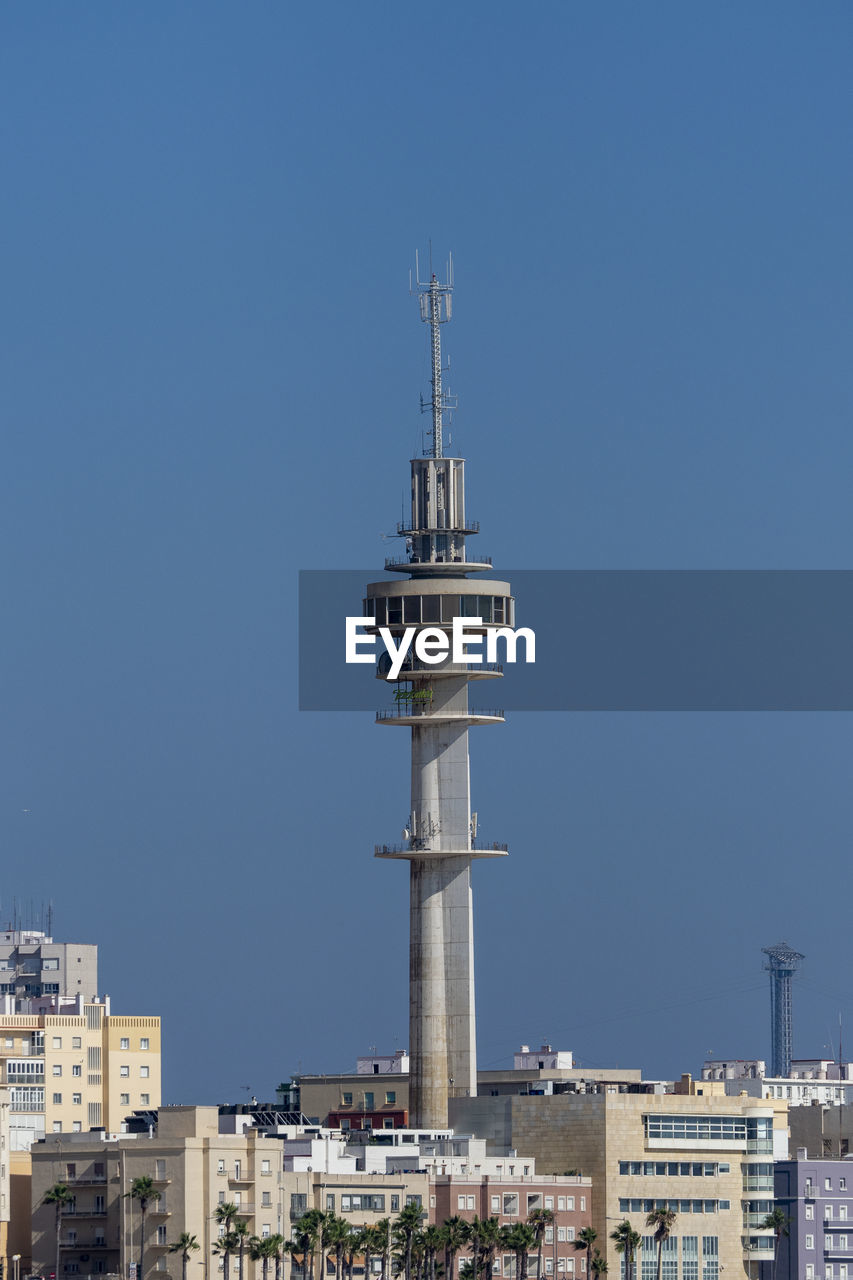 Tower amidst buildings in city against clear blue sky