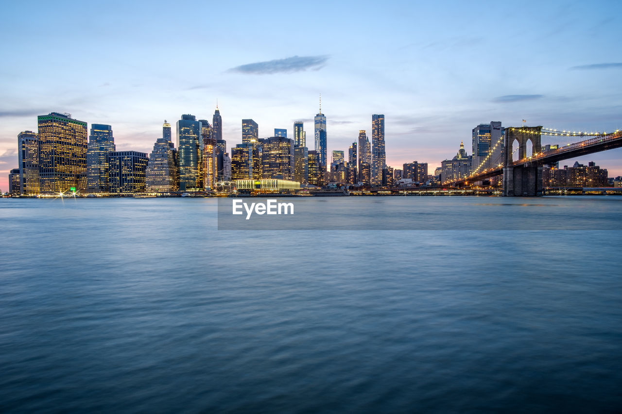 Illuminated buildings by sea against sky in city