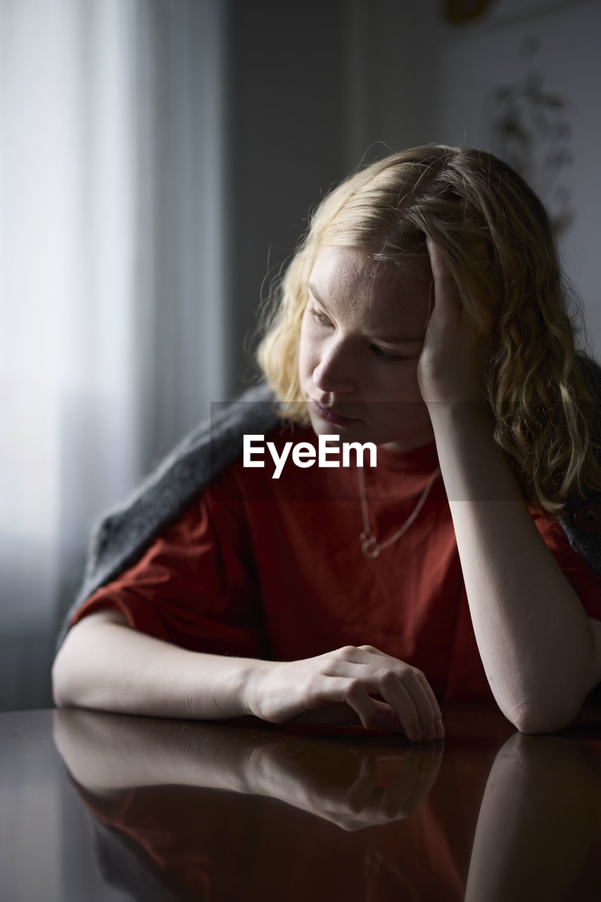 Pensive teenage girl sitting at table with head in hands