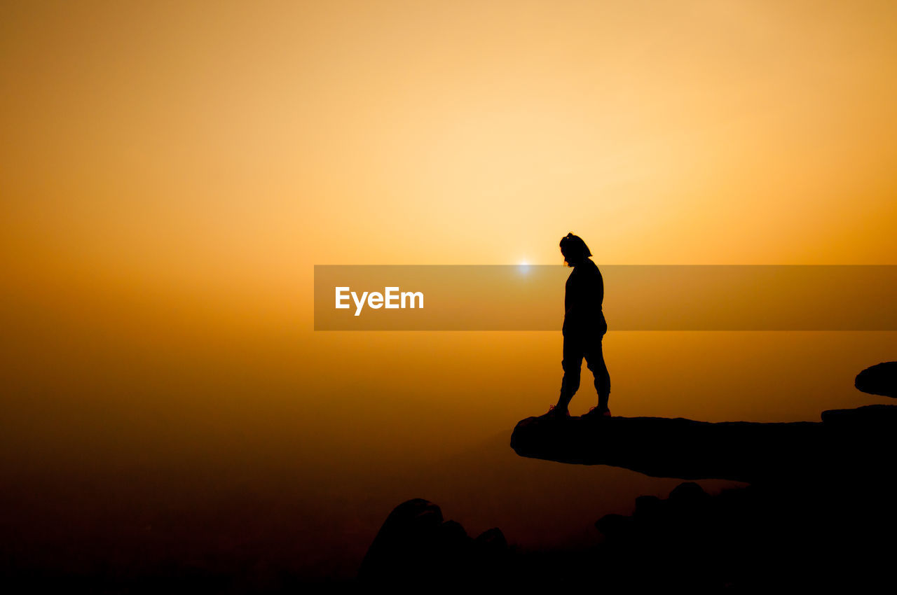 Silhouette of woman standing on cliff against sky during sunset