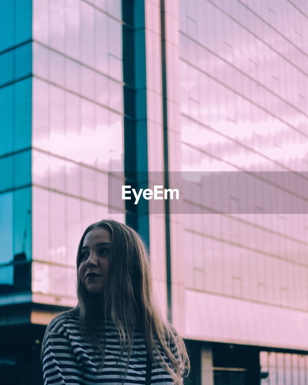 Low angle view of thoughtful beautiful woman standing against modern building