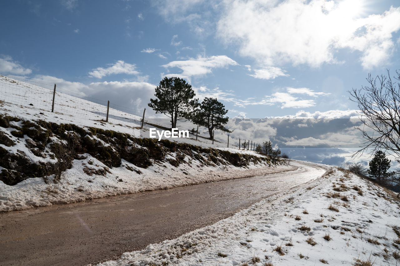 Road by snow covered land against sky