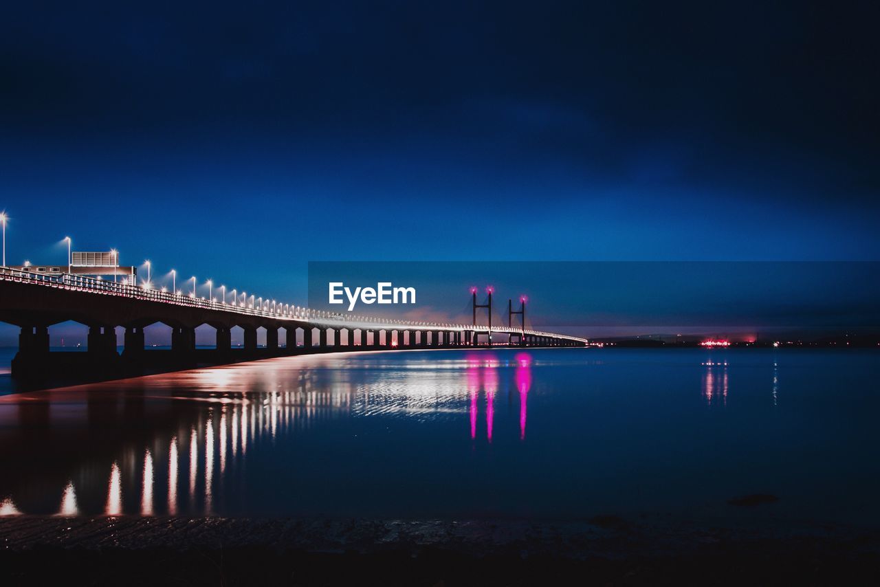 Illuminated bridge over river against sky at dusk