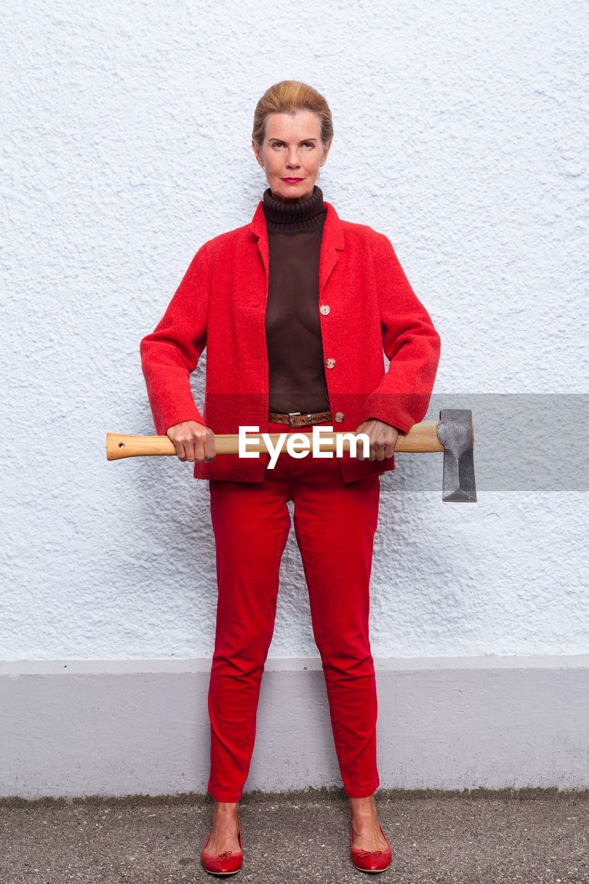 Portrait of woman holding axe standing against white wall