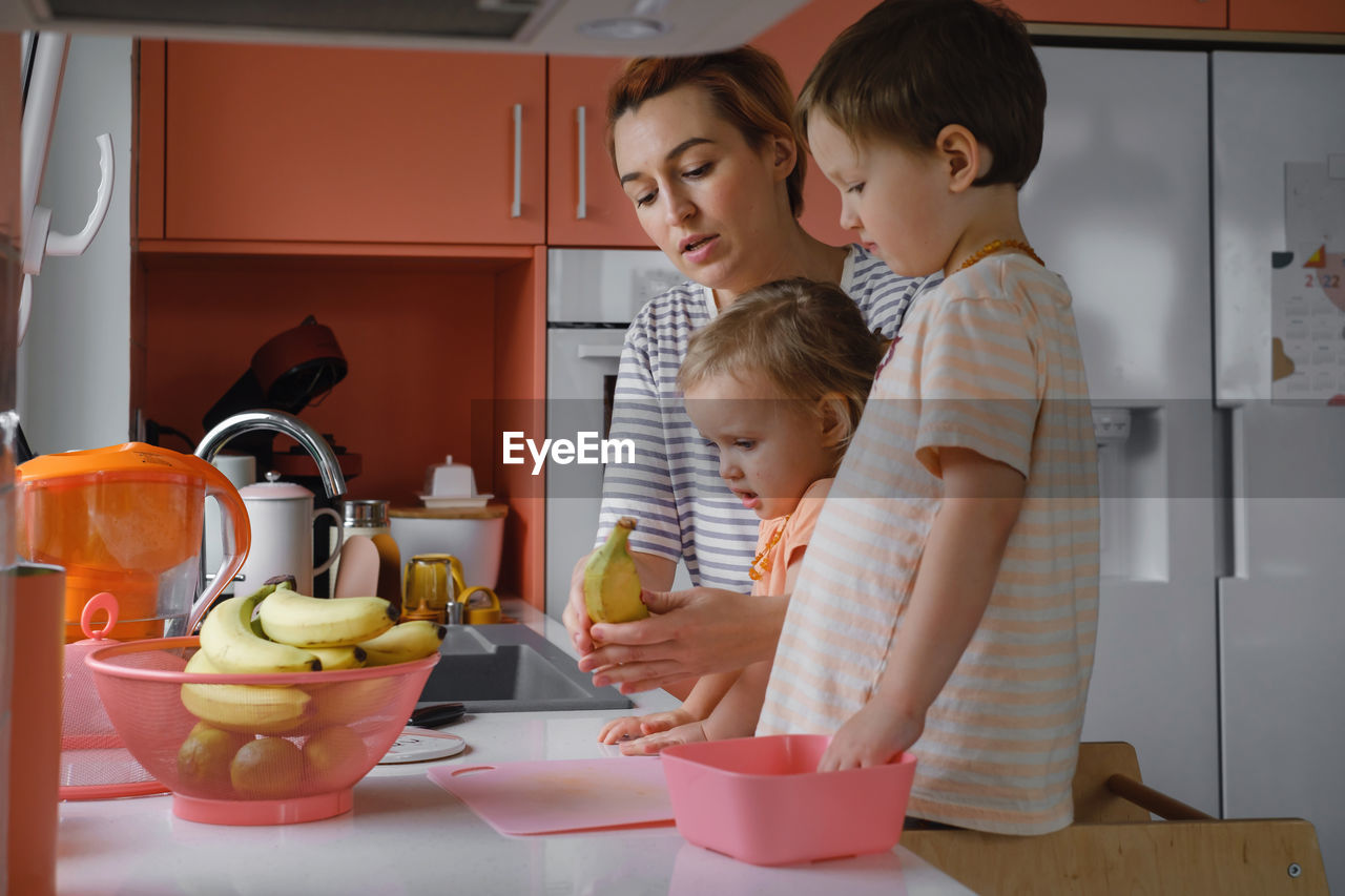 Happy family with kids cooking on modern kitchen. children cutting fruit salad, preparing food with