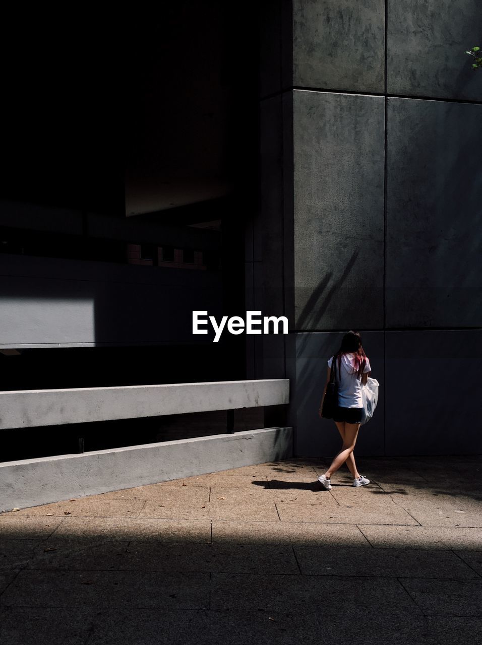 Rear view of woman walking on footpath by building