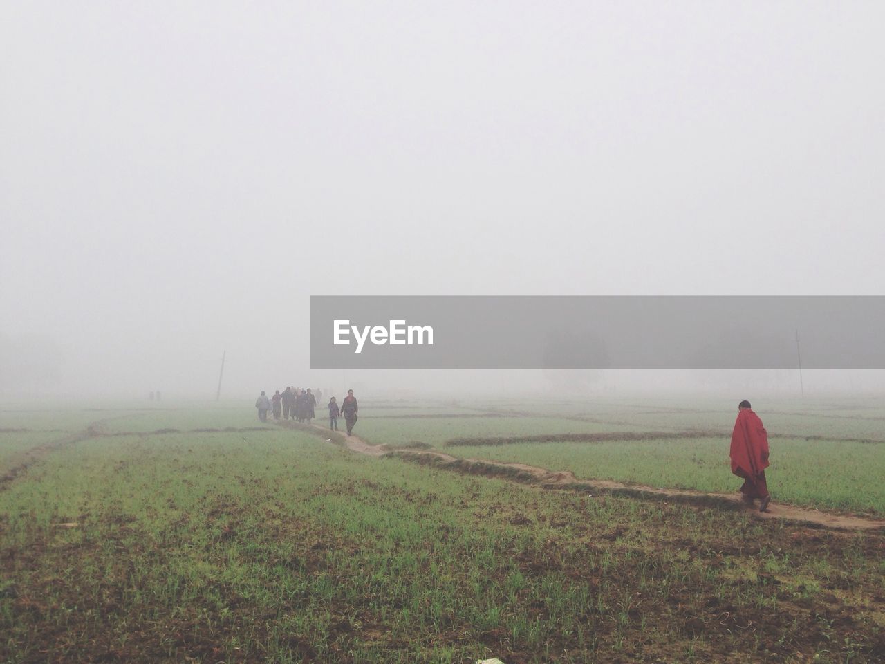 People walking on field against sky during foggy weather